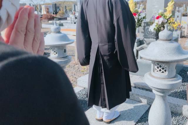 お墓の前に立つ僧侶